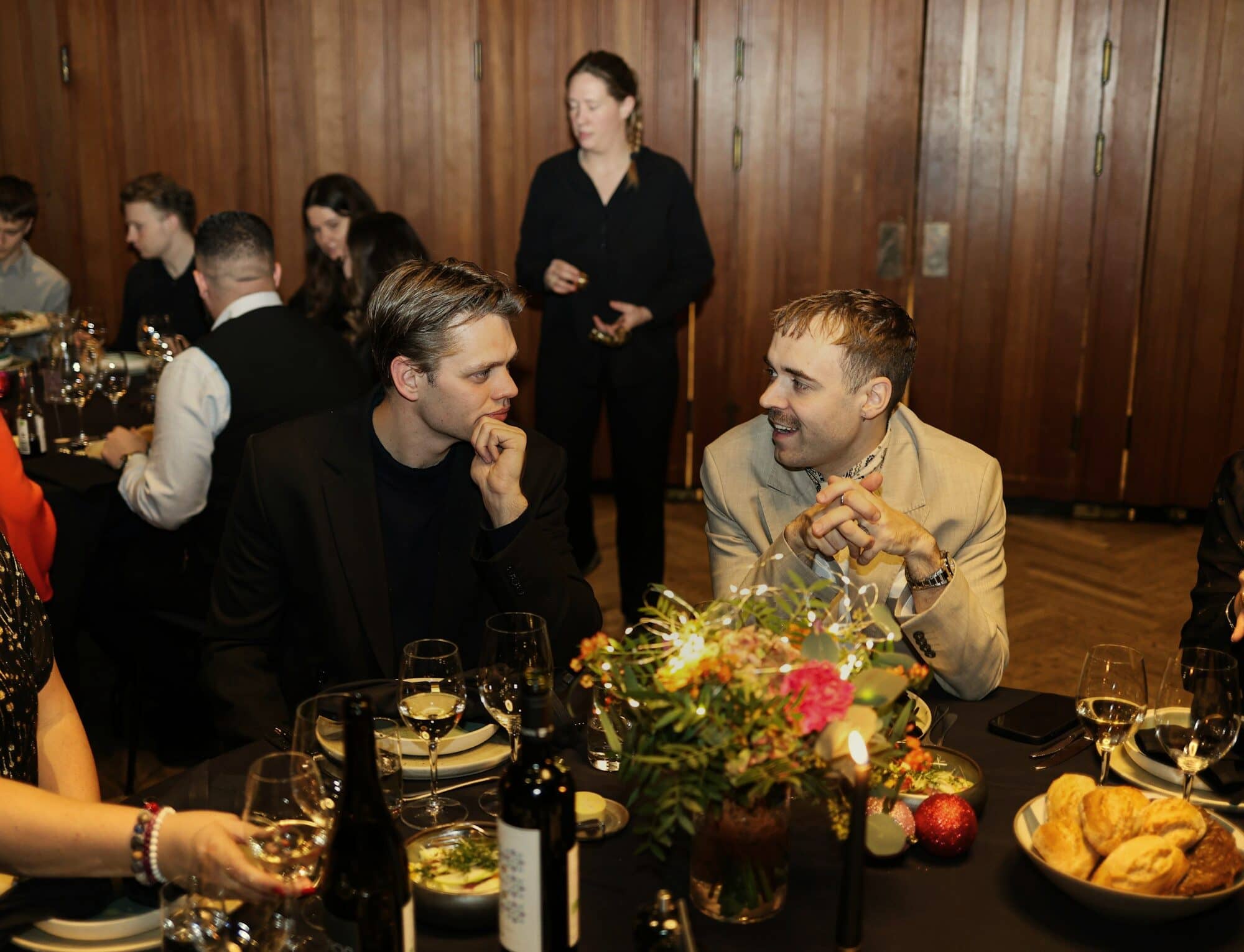 Guests deep in conversation around a dinner table with flowers, candles and wine