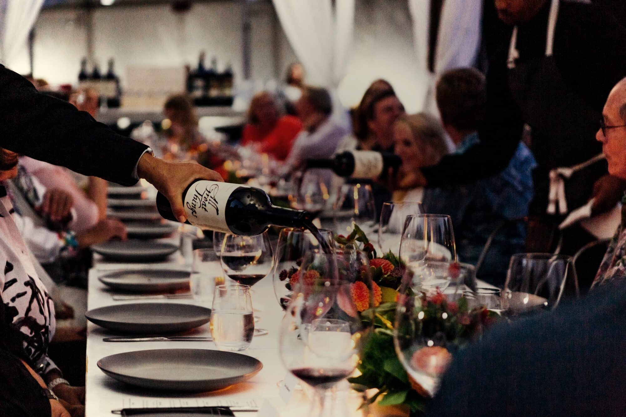 Wine being poured along a long dinner table full of guests